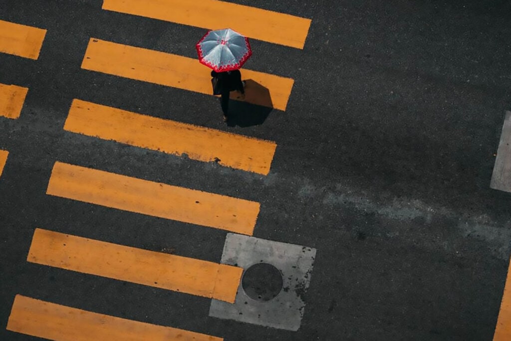Person crossing street with umbrella on rainy day, highlighting trust and safety.